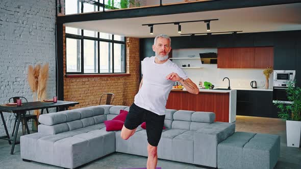 Man with Tattoos Practicing Yoga While Standing in Front of a Grey Couch with Red Cushions with a alt