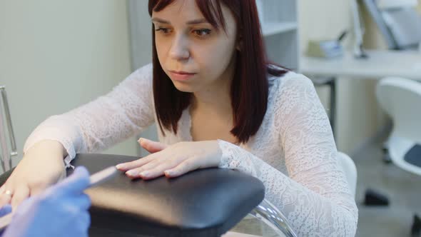 Unrecognizable Person in Gloves Saws Nails of Young Woman in Salon alt