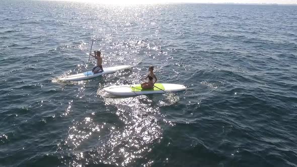 Two Caucasian Male and Female Rowing on Supboardsin Sea with Ship on Background alt