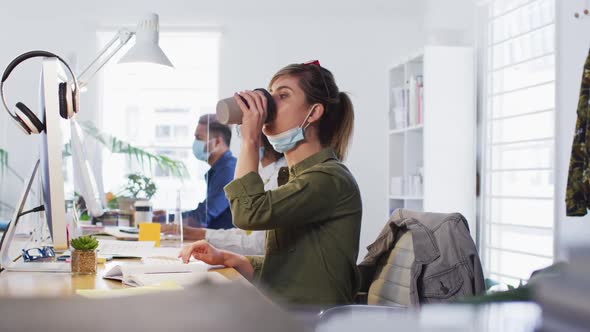 Woman drinking coffee while sitting on her desk at office alt
