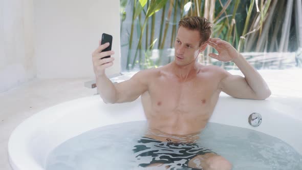 Handsome Man with Muscular Body Takes Bath Takes Selfie on Phone Smiles Winks alt