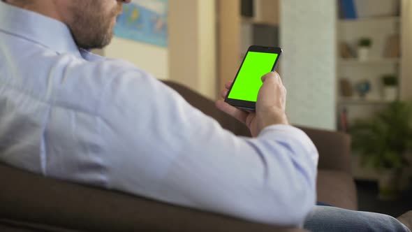 Bearded Male Sitting on Sofa and Scrolling on Cellphone With Green Screen, App alt