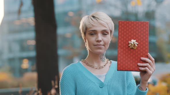 Young Woman Revealing Her Satisfied Face Behind the Gift Box in the Park alt