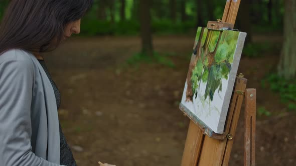 Female's Hand Painting a Landscape on Canvas in a Park. alt