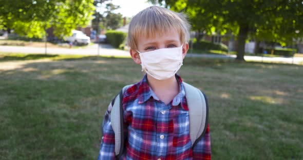 Little boy takes off his face mask in a school yard. alt