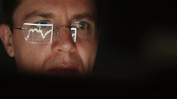 REFLECTION: Face of trader in an eyeglasses looking a graphs in a the night