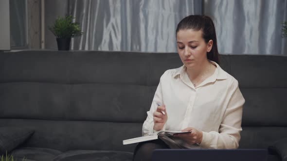 Young Woman Writing in Notebook While Sitting on Sofa in Modern Apartment.