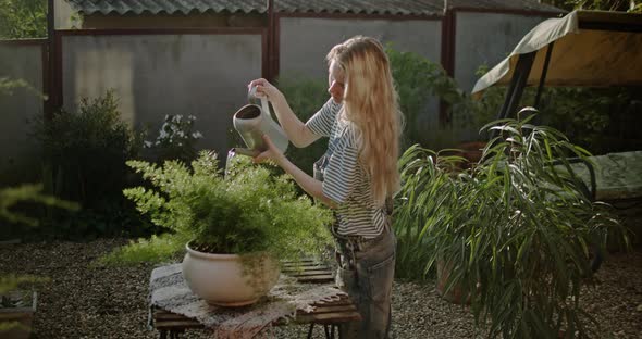 Young Girl with a Watering Can Watering Flowers in a Summer Garden at Sunset