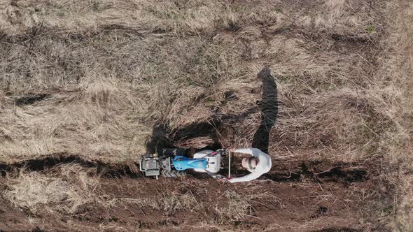 AERIAL - Man working a field with a rototiller, agriculture, wide shot pan left alt