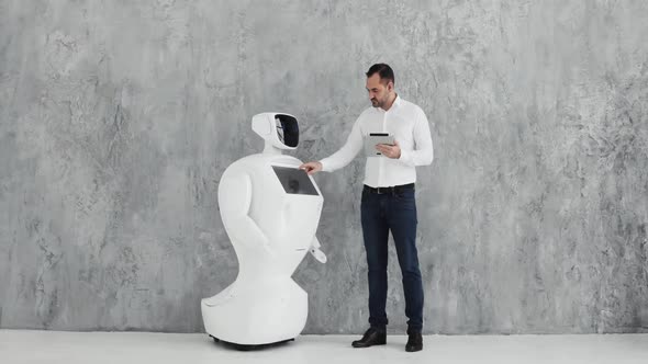A Stylish Man Communicates with a Robot, Presses a Plastic Mechanical Arm To the Robot, Handshake alt
