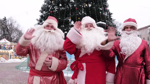 Three Santa Clauses on the Background of a Christmas Tree in the City Center alt