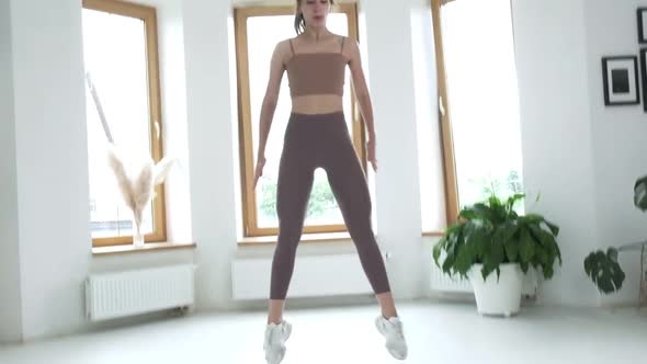 Young Fit Brunette Girl in Sportswear Does Jumps Squats in Bright Room at Home