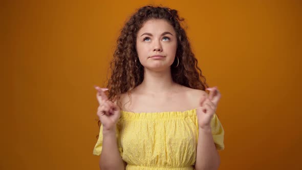 Young Praying Girl Showing Finger Sign for Good Luck Against Yellow Background