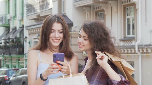 Two Cheerful Young Women Browsing Online on Smart Phone Outdoors