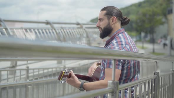 Side View of Sad Man Playing Guitar on Urban City Street. Young Poor Musician Performing on Summer alt