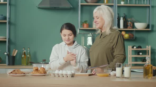 Smiling Older 60s Grandmother and Cute Granddaughter Cooking Together in the Kitchen alt