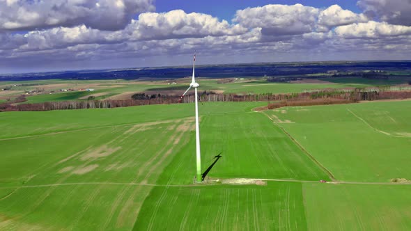 Aerial view of white wind turbine on green field in spring alt