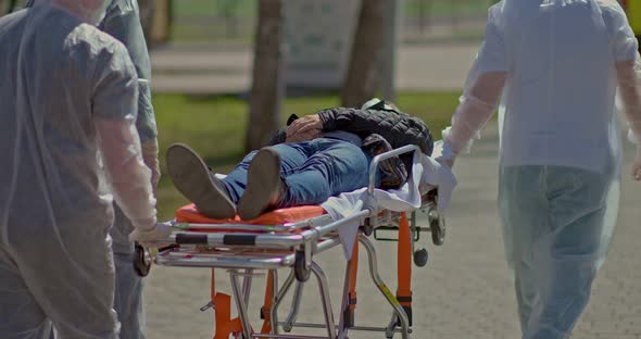 Doctors in Protective Suits Carry a Coronavirus Infected Person on a Stretcher alt