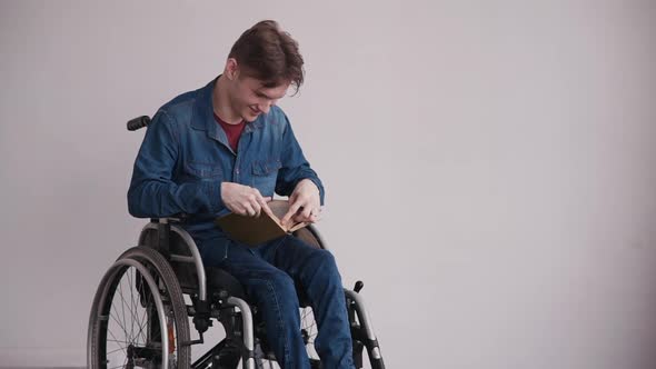 Young and Disabled Man Sitting in Comfort Wheelchair. Male Reading Book at the Hospital