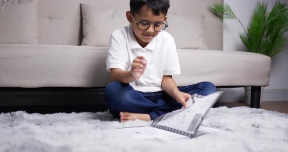 Asian boy wearing glasses sitting and practicing reading on warm floor alt