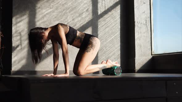 Woman with a Tattoo Uses a Roller for Warming Up Muscles in a Fitness Club alt