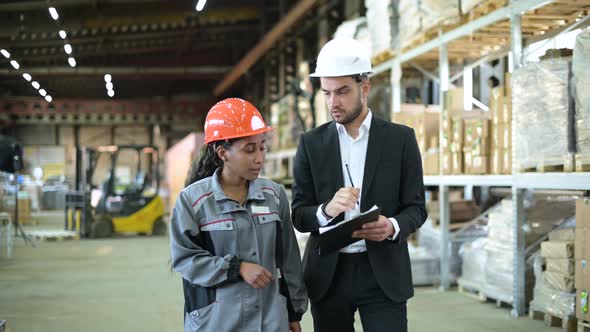 A young manager and a warehouse worker walk through the production workshop alt