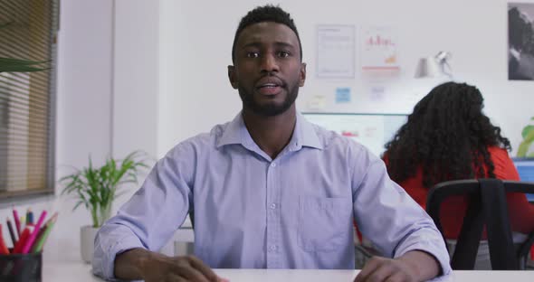 African american businessman sitting at desk, making video call in modern office alt