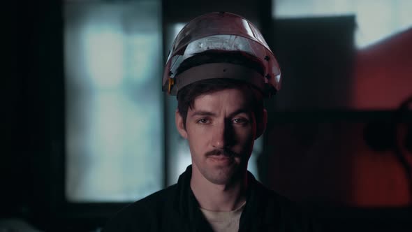 A Mustachioed Worker in a Black Shirt Stands in the Workshop and Puts Down and Puts on His Safety