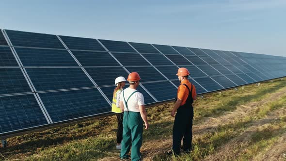 Three Employees of Alternative Power Plant Walking and Talking About Scheme of alt