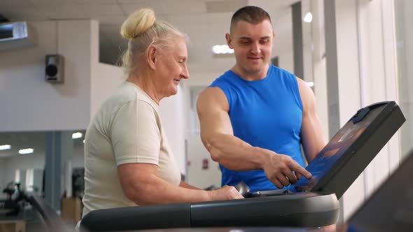 Young Handsome Coach Shows an Old Woman How to Manage a Treadmill