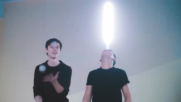 the Guy Juggles While the Other Holds the Light on His Nose
