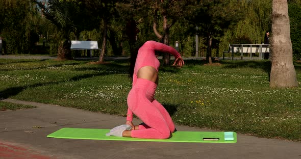 Young woman doing yoga practice or stretching on green grass in park.