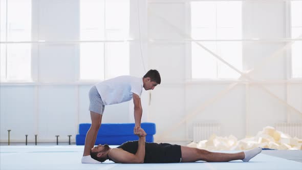 A Fit Man and a Teenager are Practicing Acrobatic Handstand in Gym alt