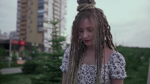 A Cute Young and Happy Girl with Dreadlocks Walks Down the Street and Poses