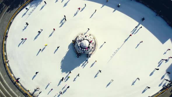 Many People are Skating on White Outdoor Ice Rink in City on Sunny Winter Day alt