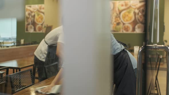 Waiter wearing protective face mask while cleaning tables in restaurant