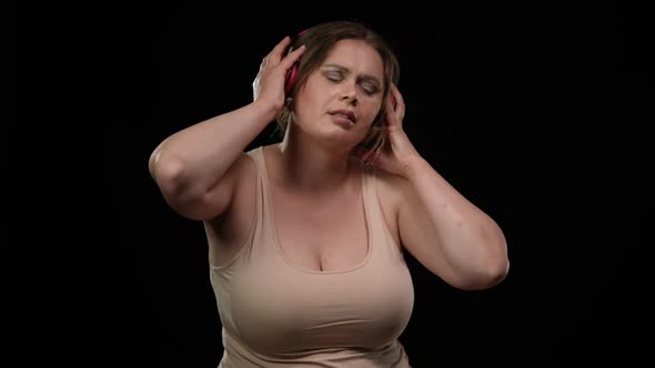 Carefree Cheerful Plus Size Woman in Headphones Dancing Listening to Music at Black Background alt