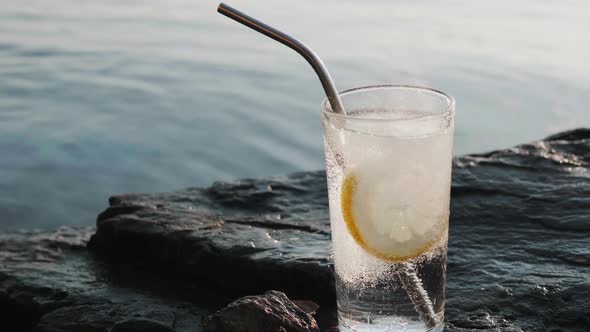 Round Slice of Lemon Falls Into a Glass of Soda Soda Water on Rocky Shore alt