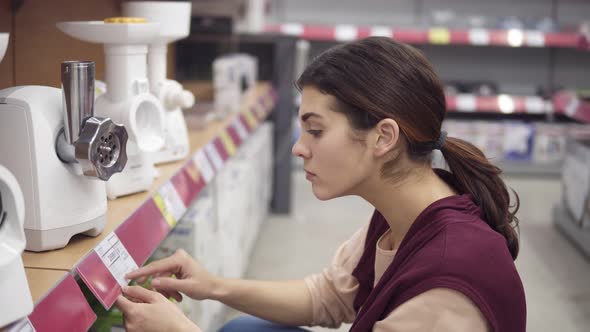 Young Female Costumer Comparing Prices for Electrical Meat Grinders Looking for Perfect Kitchenware alt
