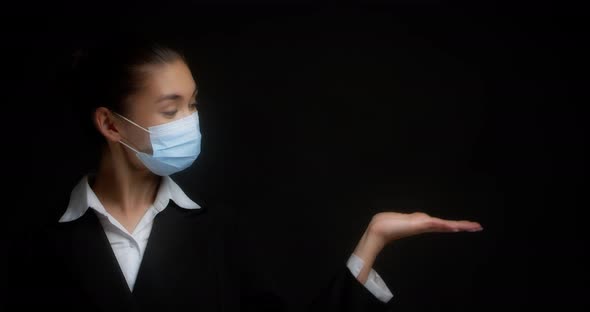 Business Woman in a Medical Mask Points with Her Palm to an Empty Copy Space