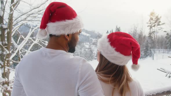 Happy Young Couple with Christmas Hats Enjoying Snowfall on the Mountain alt