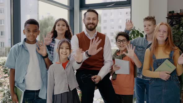 Male Teacher with Middle School Children Looking at Camera and Waving Hands alt