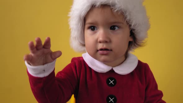 Cute Happy Cheerful Chubby Toddler Baby Girl in Santa Suit Looking On Camera At Yellow Background alt