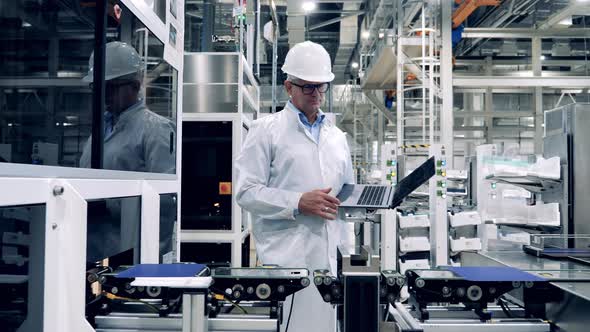 Factory Inspector with a Laptop is Observing Production of Solar Cells alt