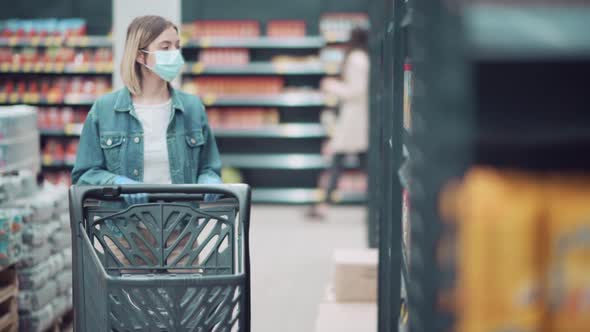 Lovely Blonde Girl in a Medical Mask Takes Goods From Shopping Racks