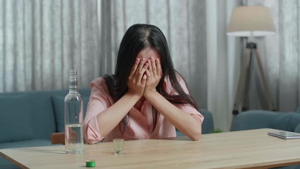 Drunk, Depressed Asian Woman With Smartphone On Table Pouring Vodka In A Shot Glass Before Drinking alt