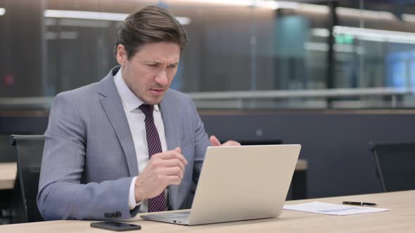 Middle Aged Businessman with Laptop having Headache in Office  alt
