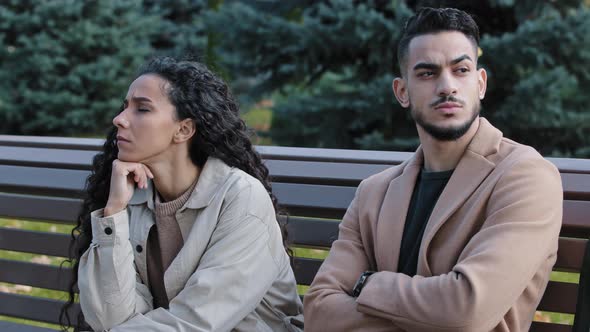 Offended Young Hispanic Couple Looking Different Direction Sitting on Bench in Autumn Park Annoyed alt