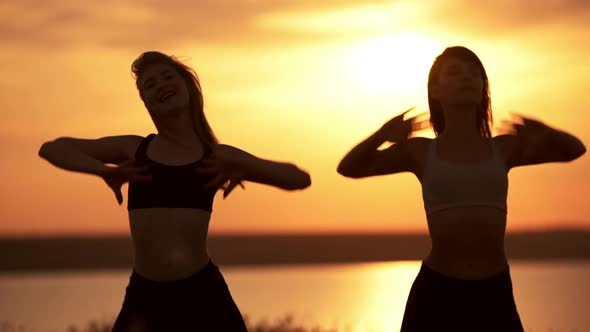Silhouettes of Two Beautiful Girls Dancing Zumba in Field at Sunrise alt