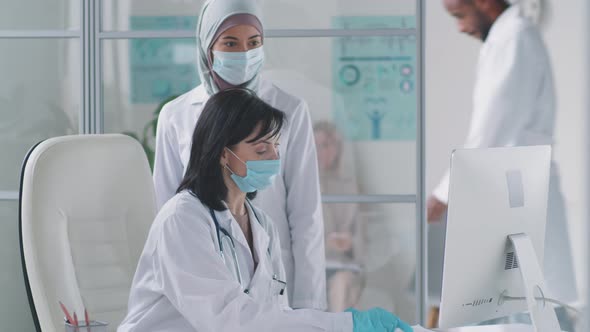 Multiethnic Female Doctors in Masks Using Computer and Talking alt